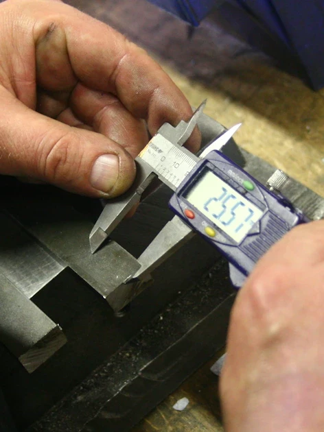 Technician using a digital caliper to measure a machined metal part — a sign it may be time to switch calibration providers