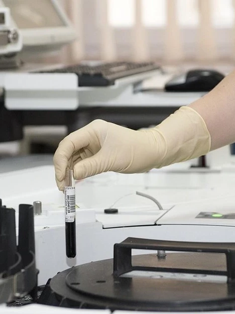 Laboratory technician handling a traceable sample tube at an analytical instrument, the accredited work behind calibration data