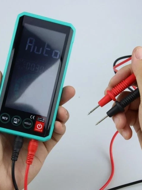 Technician holding a digital multimeter, a calibration-grade instruments, while connecting red and black test leads before taking a reading