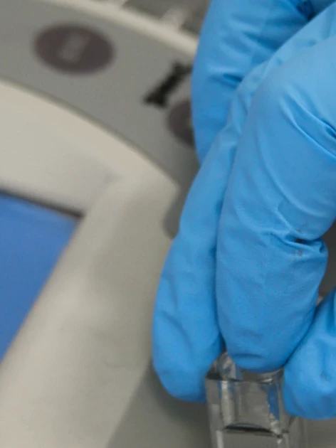 Gloved laboratory technician inserting a sample vial into a spectrophotometer during spectrophotometer calibration